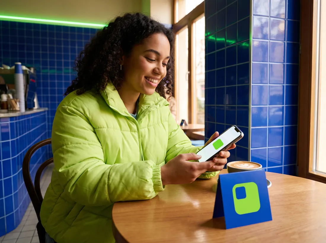A woman in a lime jacket scans the lime mark on a café table card and smiles at a simple page with one big button