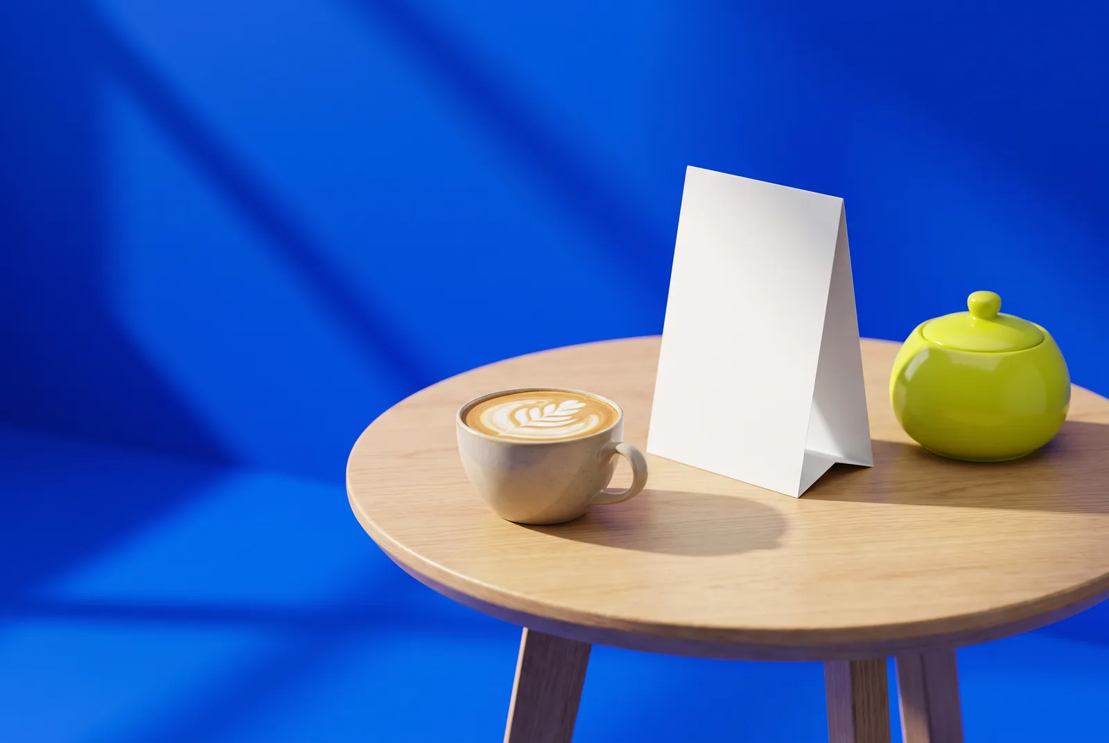 A latte with leaf art beside a blank table tent and a lime-green sugar bowl on a café table, ready for new table QR codes.