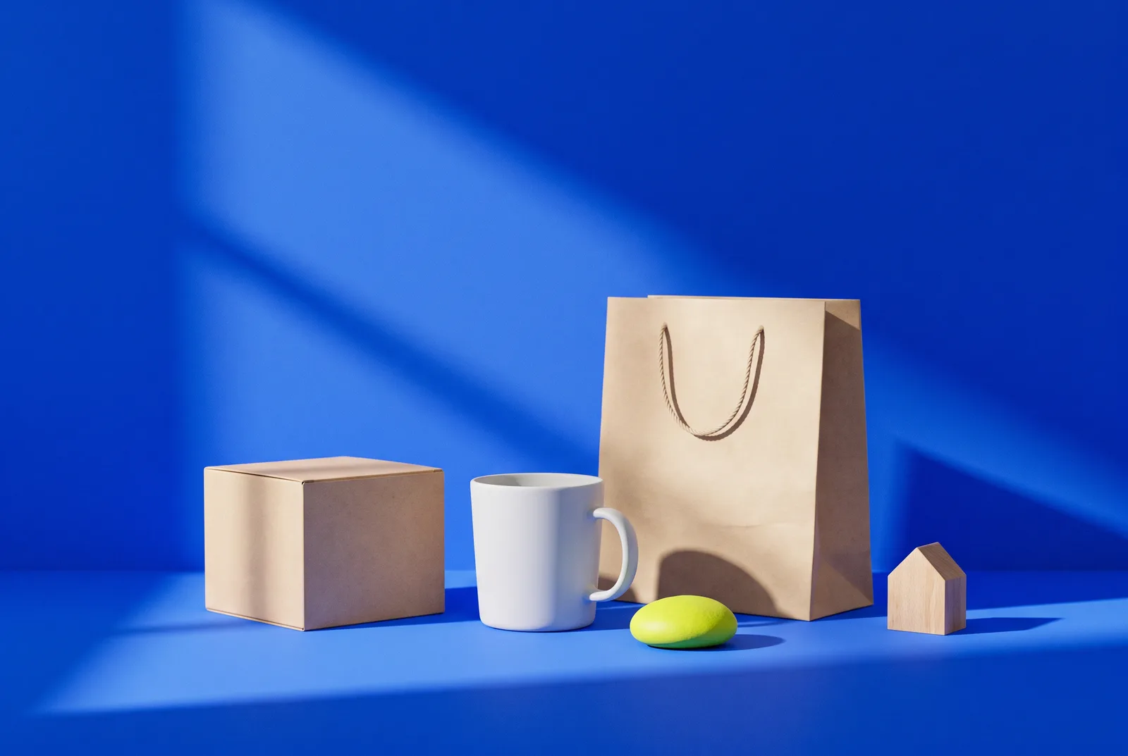 Creative QR code ideas in one still life: a plain product box, a mug, a paper shopping bag and a small wooden house on cobalt blue with a lime accent.