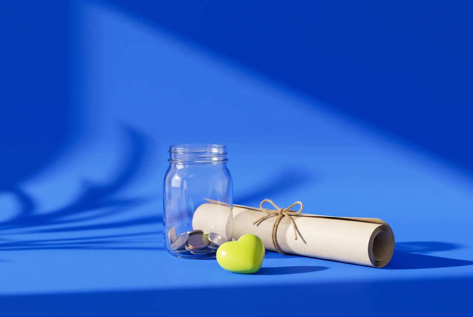 A glass donation jar with a few coins, a rolled poster tied with twine and a lime ceramic heart, the start of a donation QR code campaign.