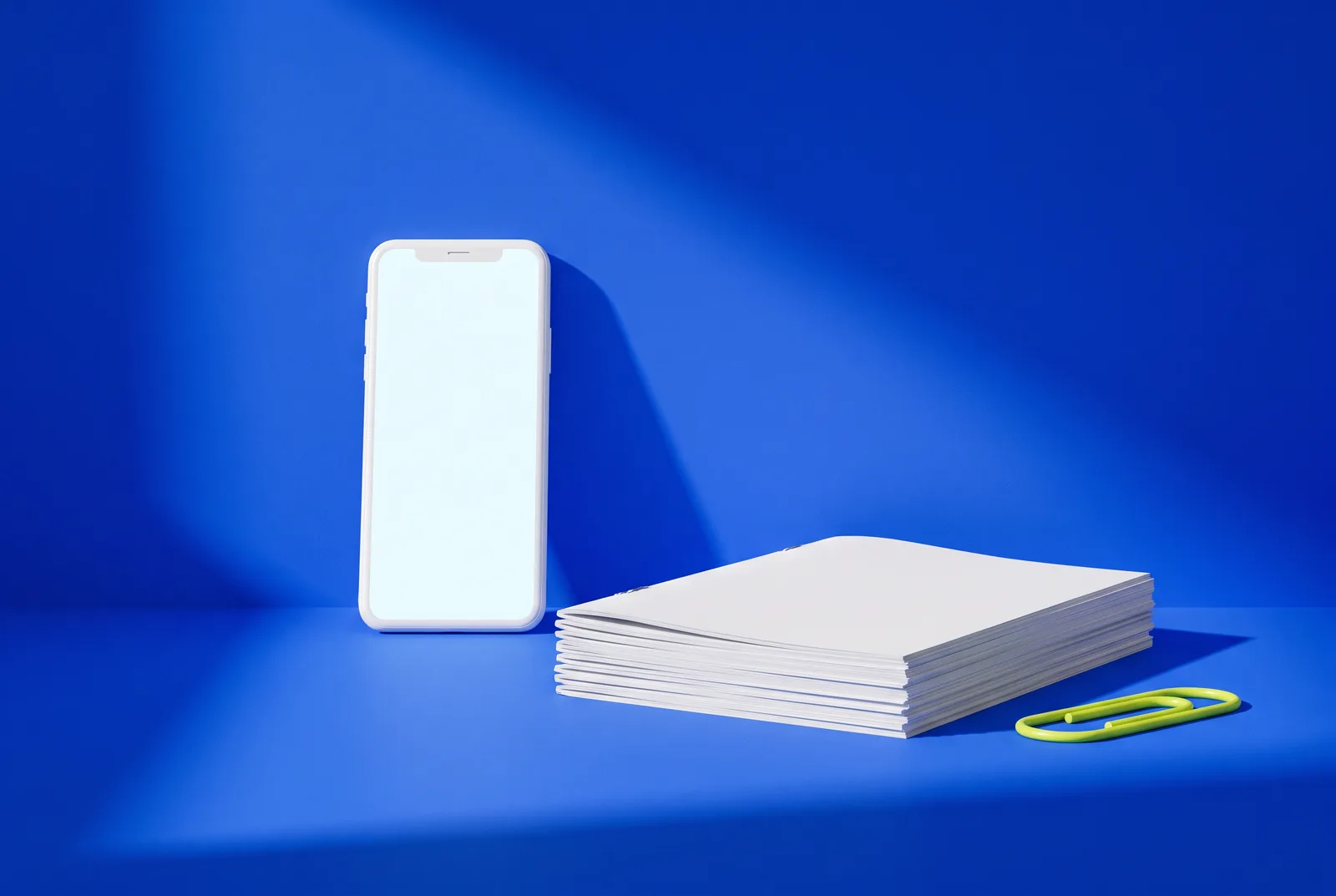A white smartphone beside a thick stack of stapled pages and a lime paperclip on a cobalt blue backdrop, the choice between a QR code PDF vs landing page.