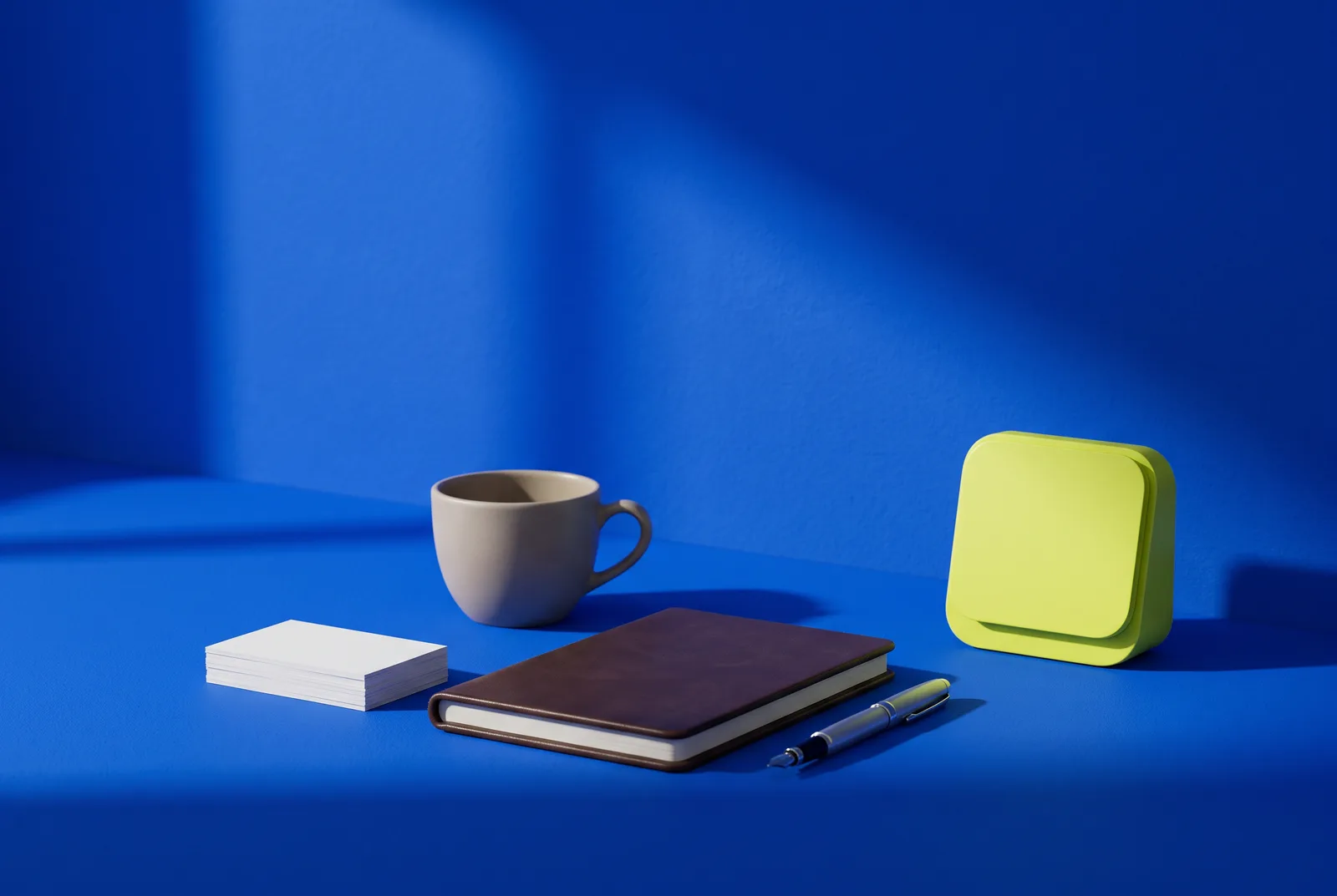 QR codes for coaches: a stack of blank business cards, a leather notebook, a pen, a coffee cup and a lime desk calendar on a cobalt blue desk.