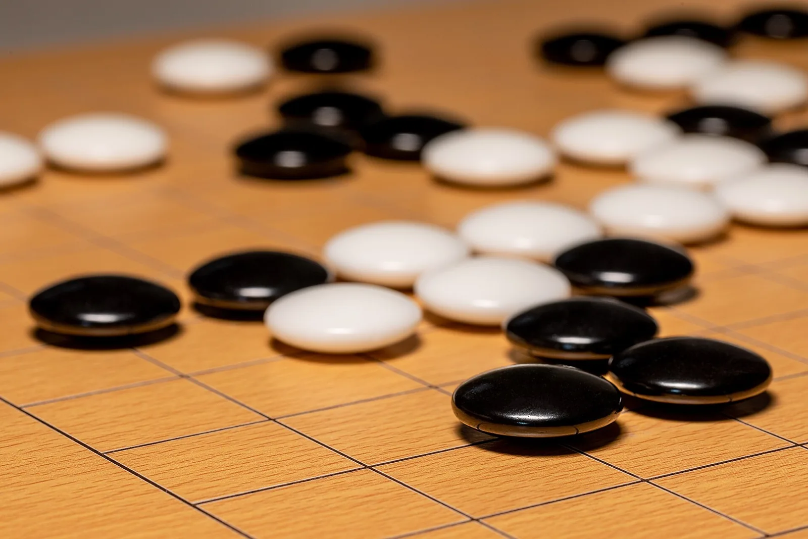 Black and white Go stones on a wooden Go board, close up.