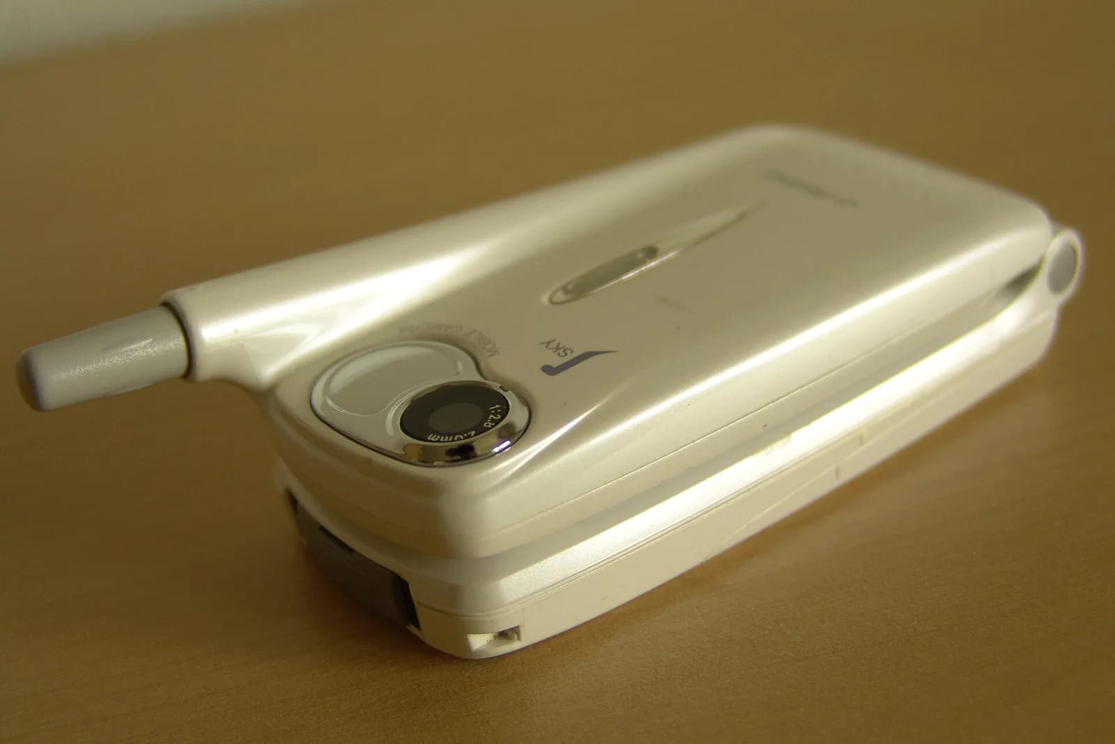 A white Sharp J-SH07 flip phone with its camera lens on the back.