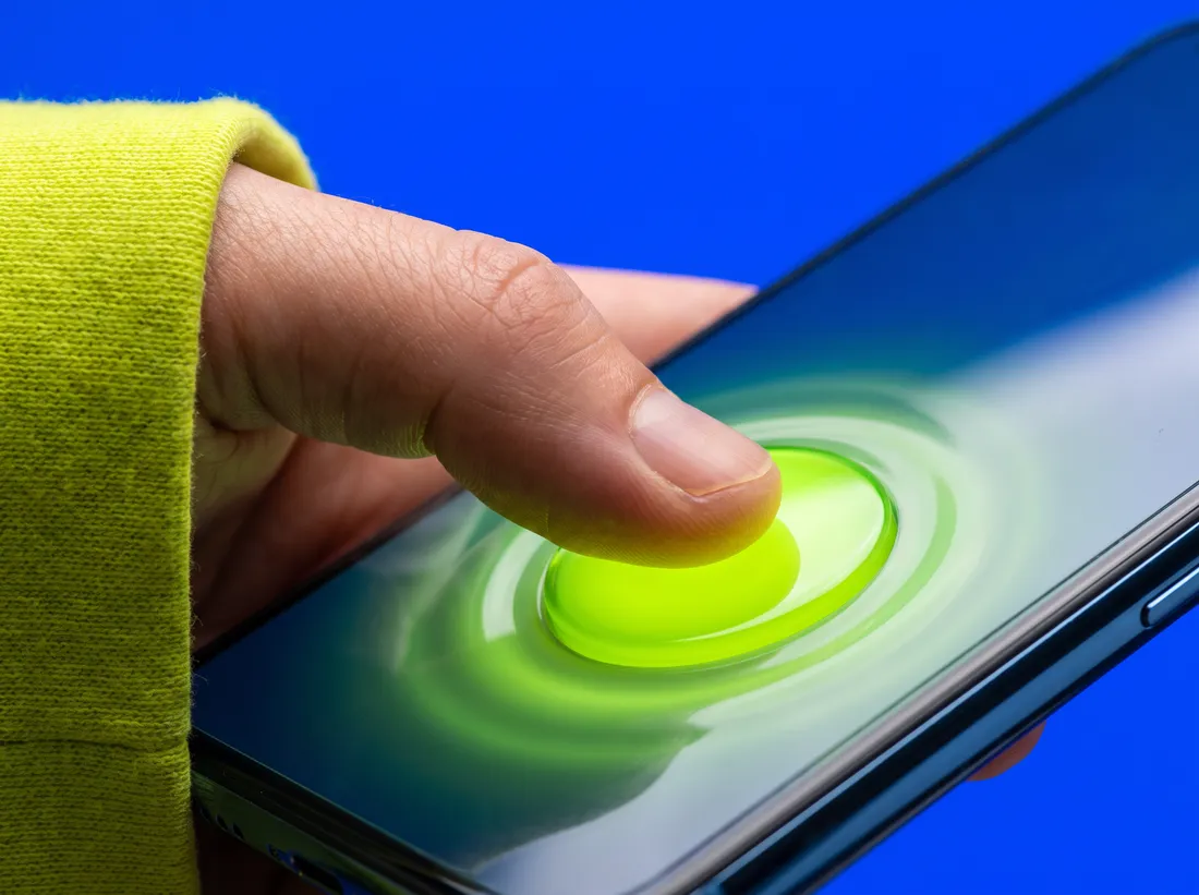 A thumb in a lime sleeve presses a glowing lime button on a phone screen, against cobalt blue
